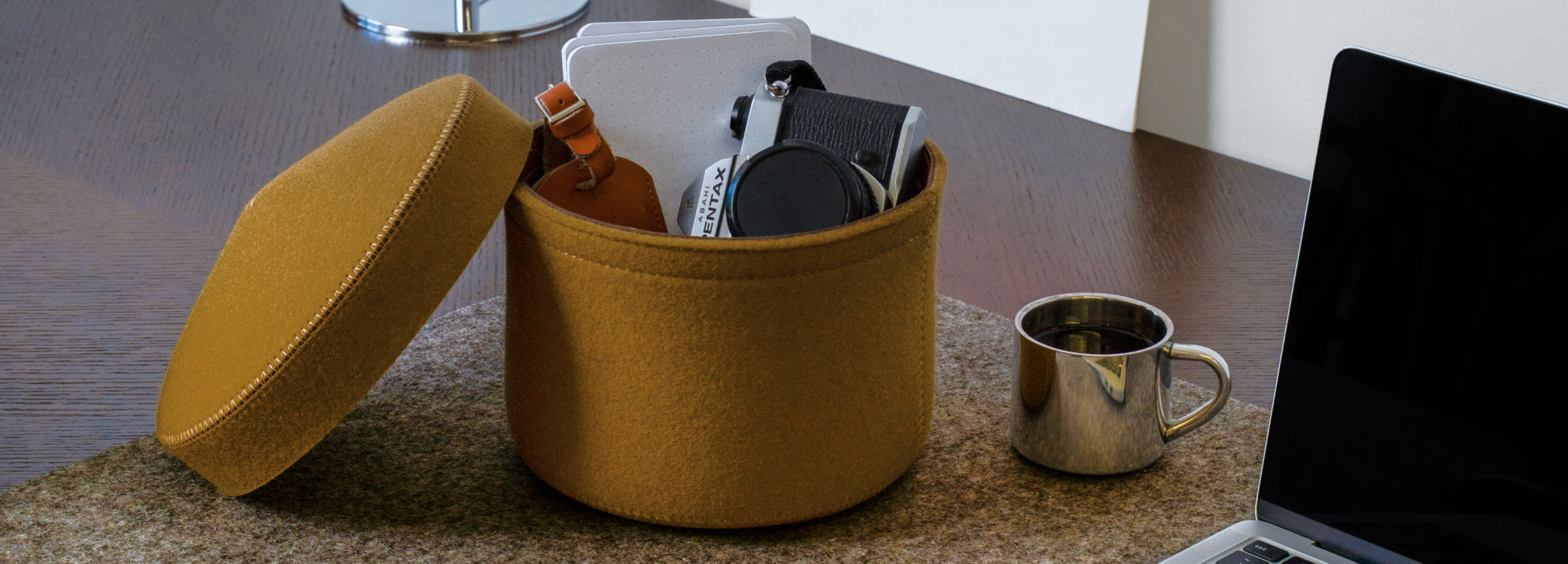 Two pairs of sunglasses, one black and one tortoiseshell, rest in a felt-lined tray on a wooden surface next to a keychain and a green plant.
