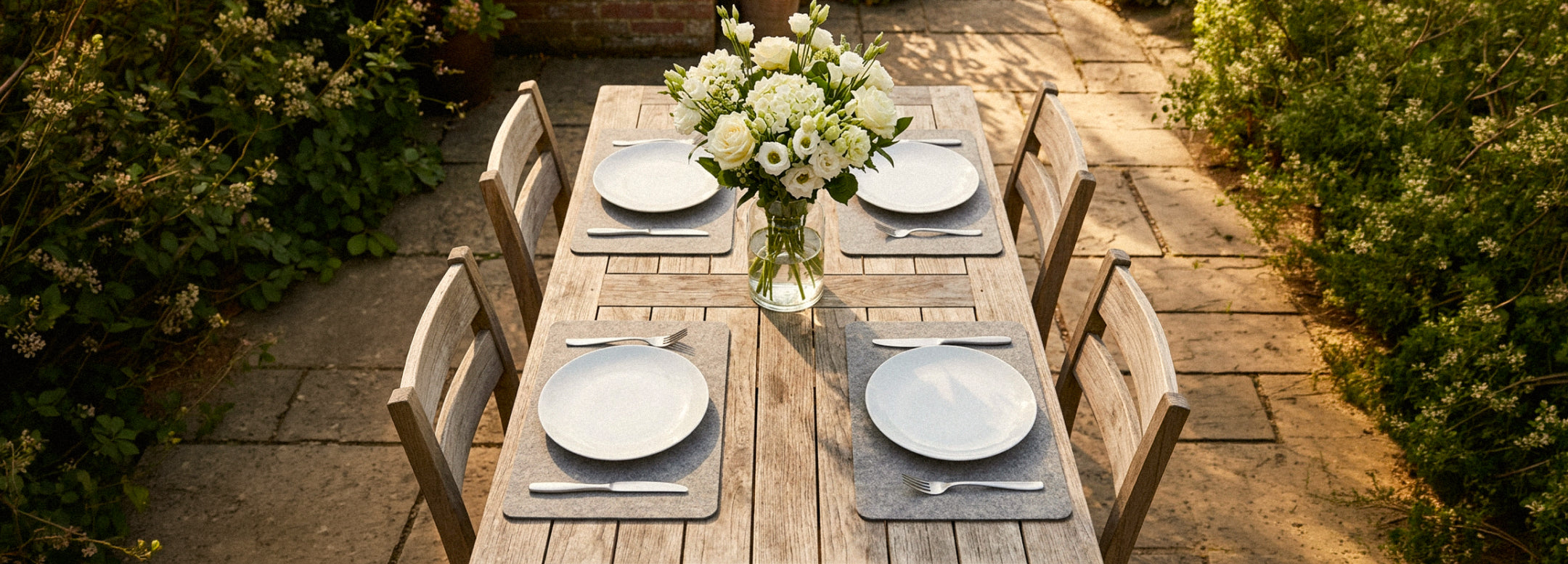 A table with four place settings features various pastries, a bowl of yogurt with fruit, glasses of water, and a persons arm reaching for food. Plates are on brown placemats.