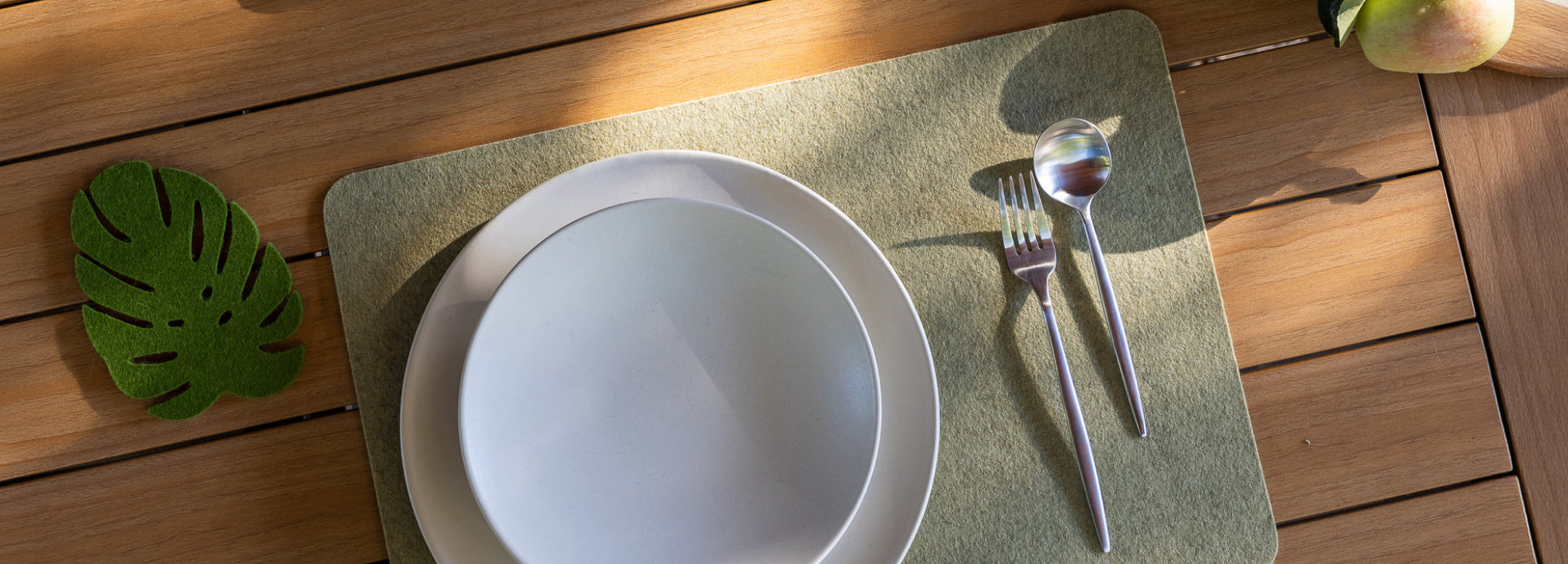 Aerial view of a dining table with navy placemats, white plates, and wine glasses. Hands reach for a charcuterie board and one pours white wine. The setting has neutral tones and elegant tableware.