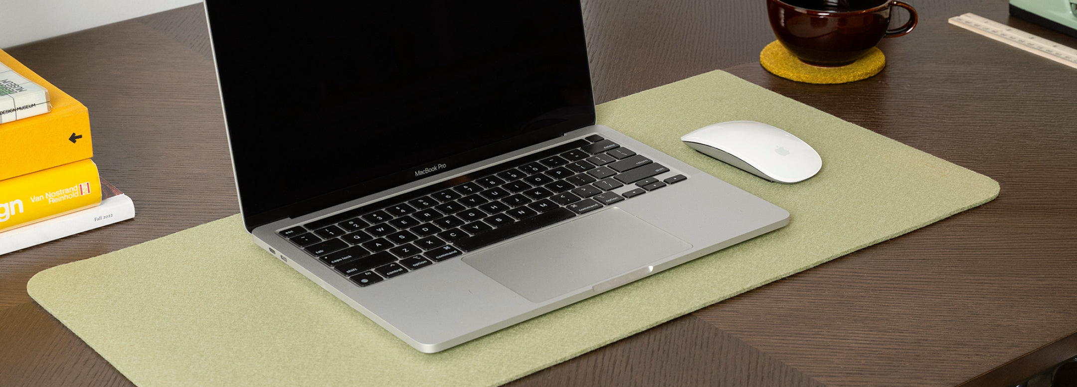 A felt sleeve with a leather flap lies next to a tray holding two pencils, an eraser, and a metal binder clip on a light wooden surface in sunlight.