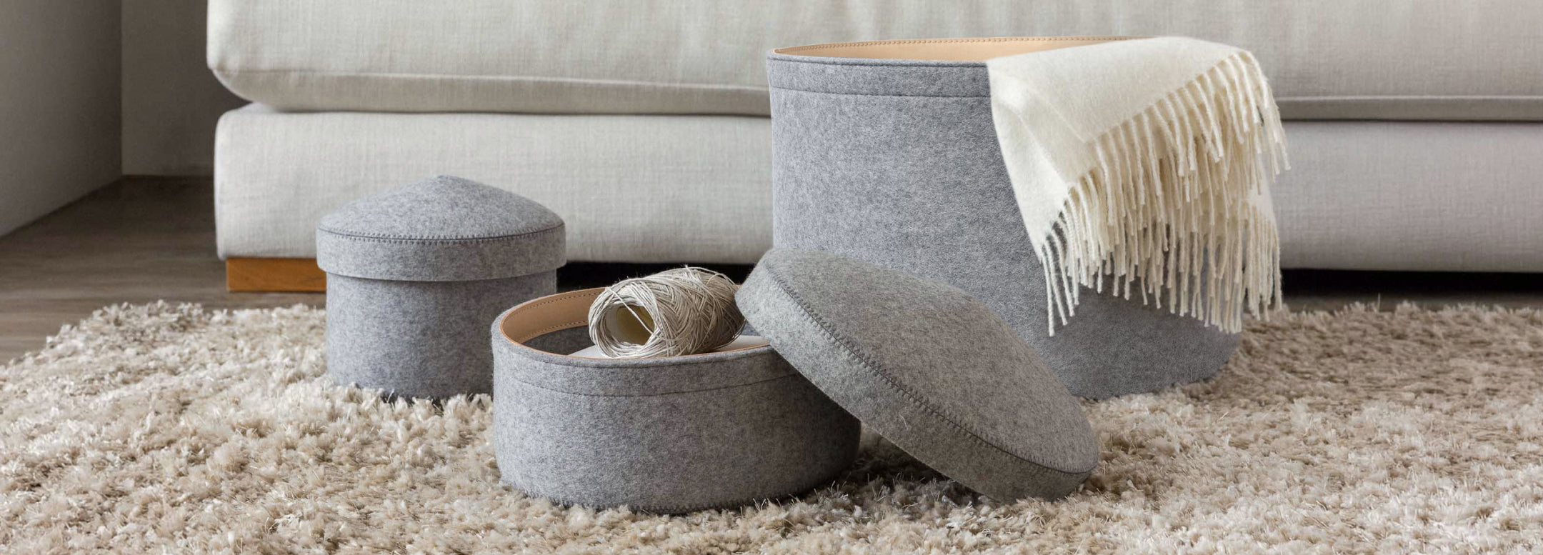 Two gray felt storage containers on a bathroom counter. One is open, holding a pouch and a small bottle. The other is closed, placed beside a bathtub. Soft textures create a cozy, minimalist feel.