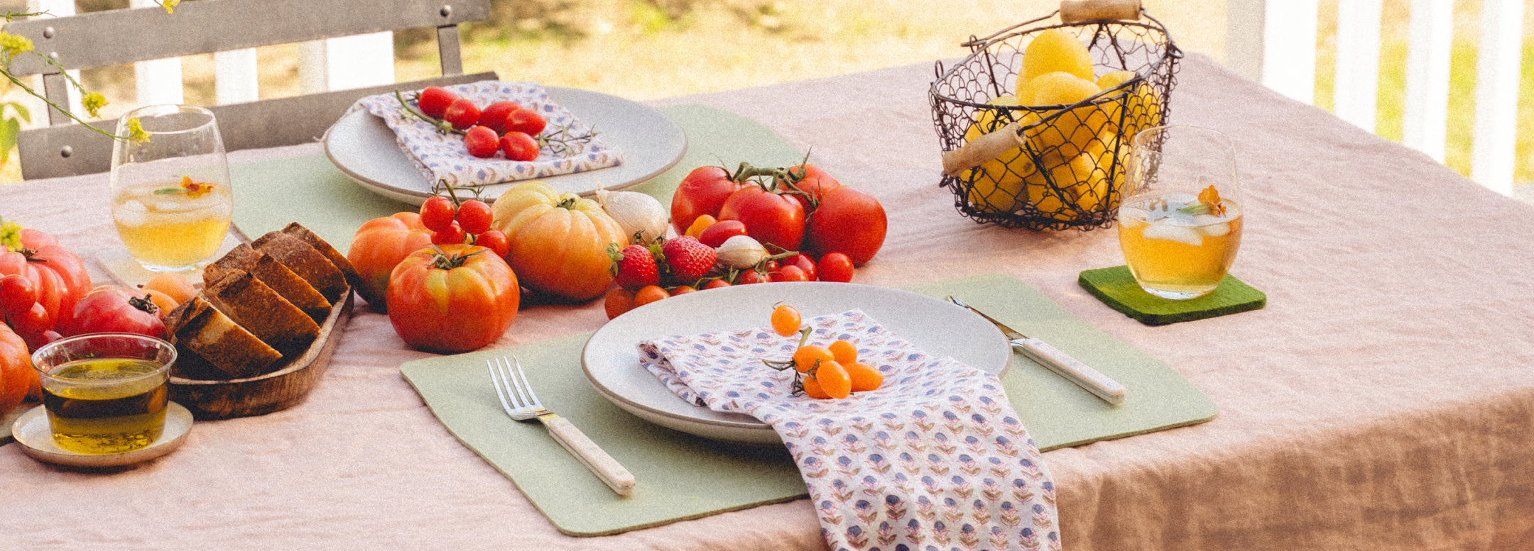 A person paints eggs at a table outdoors, surrounded by markers, a bowl of colorful eggs, fruit, lemons, and a drink. Bunny-shaped mats are on the table, adding a festive touch.