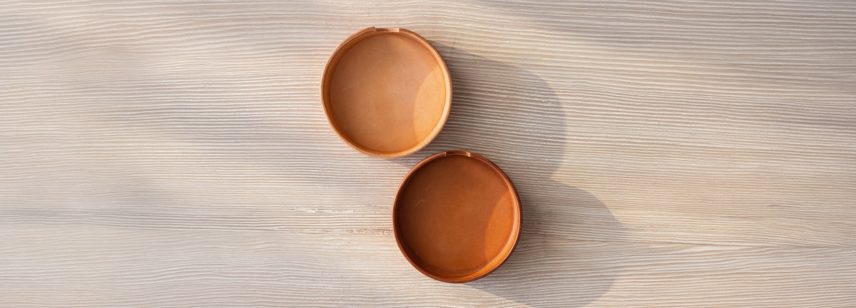 Two empty, circular wooden bowls of different shades sitting on a light wood surface.
