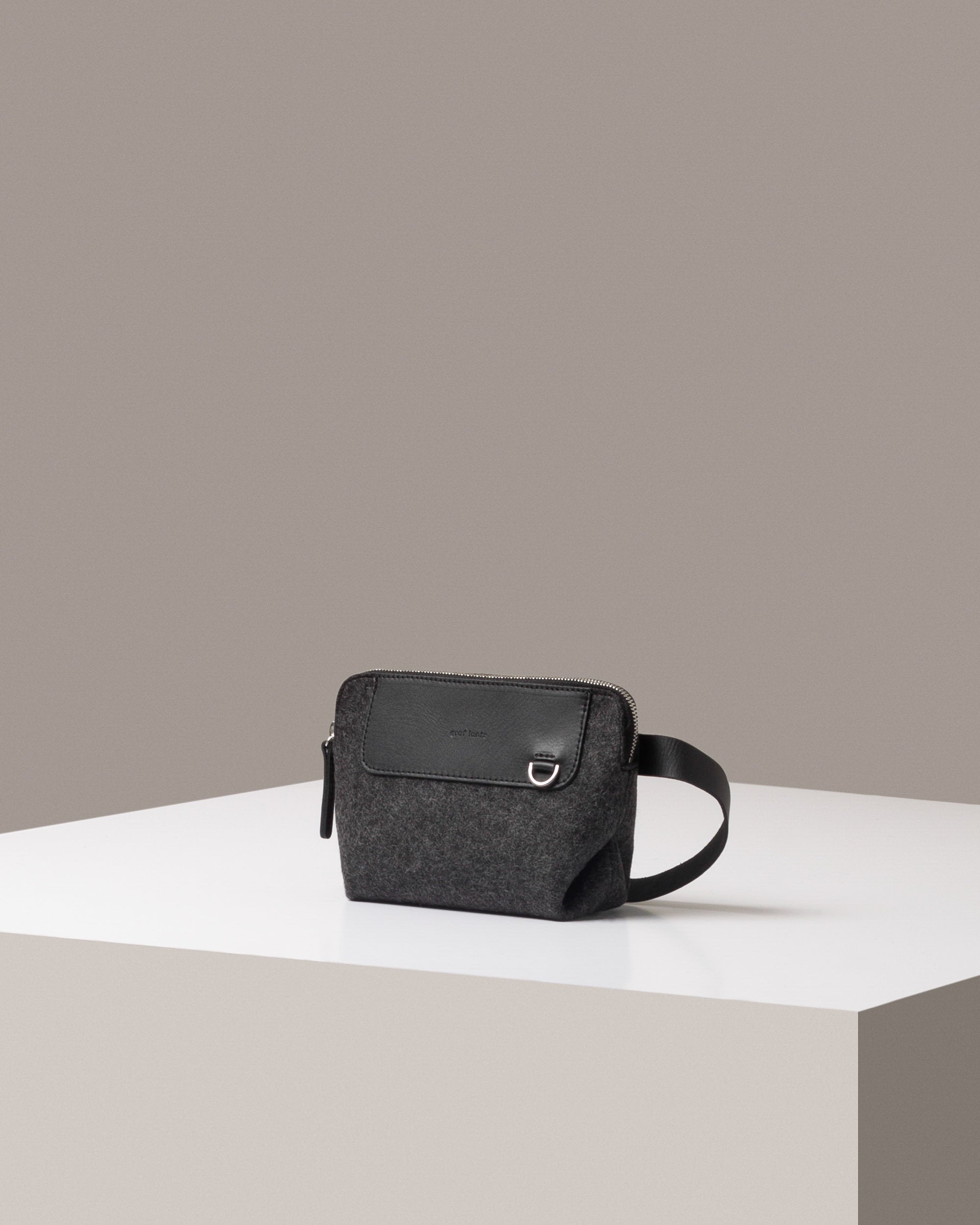 A stylish Bedford Merino Wool Felt Belt Bag in dark gray, displayed in a three-quarter view on a white base