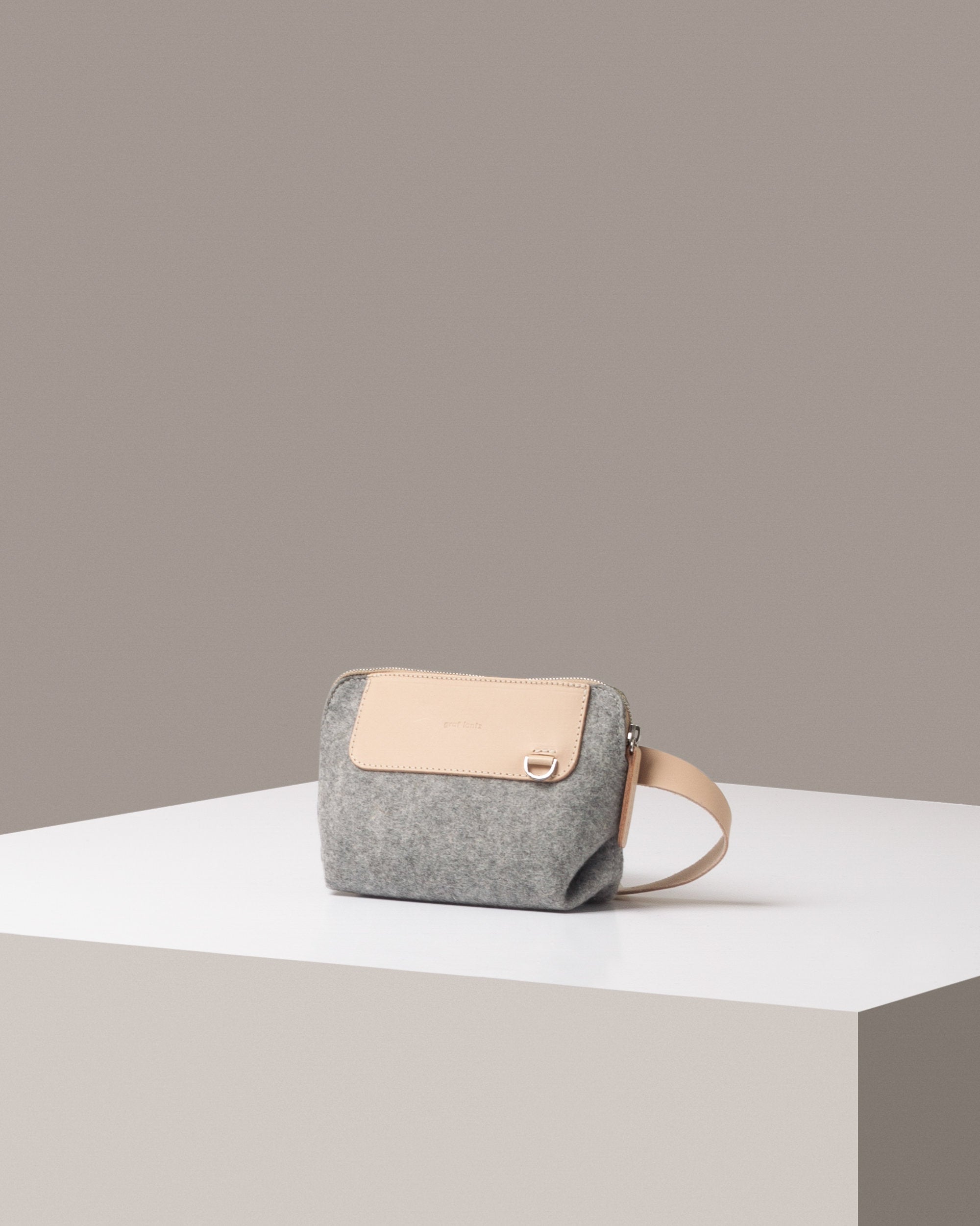 A stylish Bedford Merino Wool Belt Bag in light gray with beige leather accents, displayed in a three-quarter view on a white base