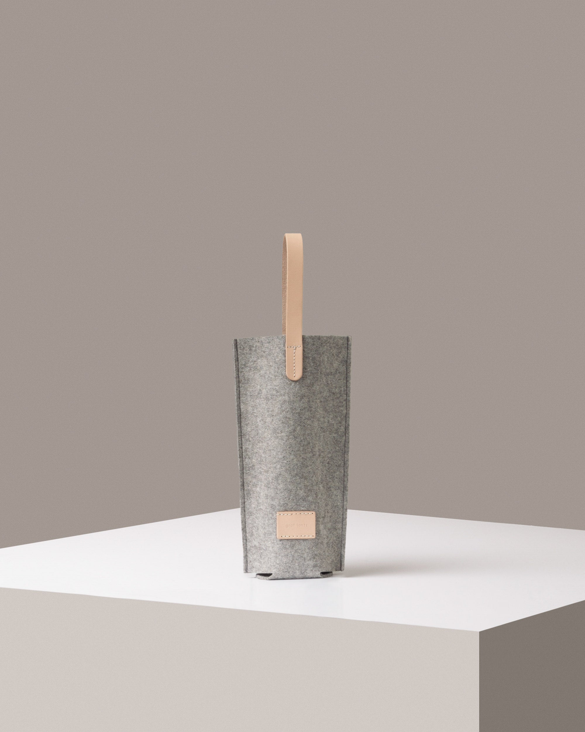 A Hana Merino Wool Bottle Bag light grey standig on a white base, front view