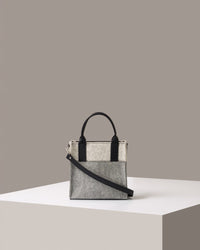 A small Merino Wool Felt Tote bag in white and grey, with black accents shoulder strap standing on a white base, front view