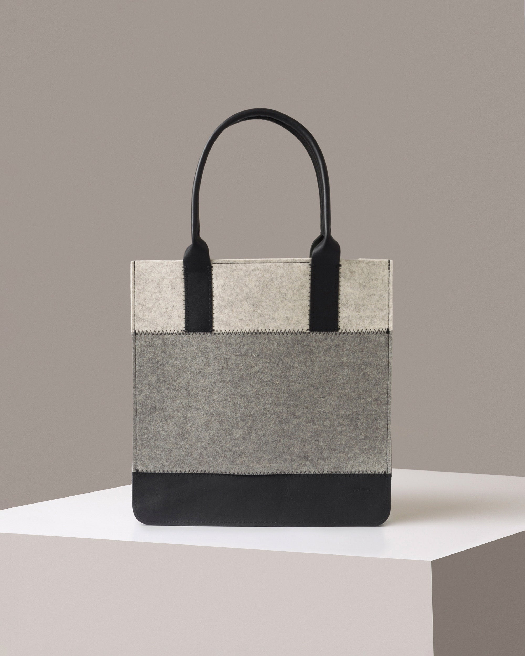A Jaunt Merino Wool Felt Tote by Graf Lantz in gray, white, and black colors standing on a white base, front view
