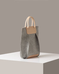 A Frankie Merino Wool Felt Tote in a grey color with beige leather accents on a white base displayed in a side-view