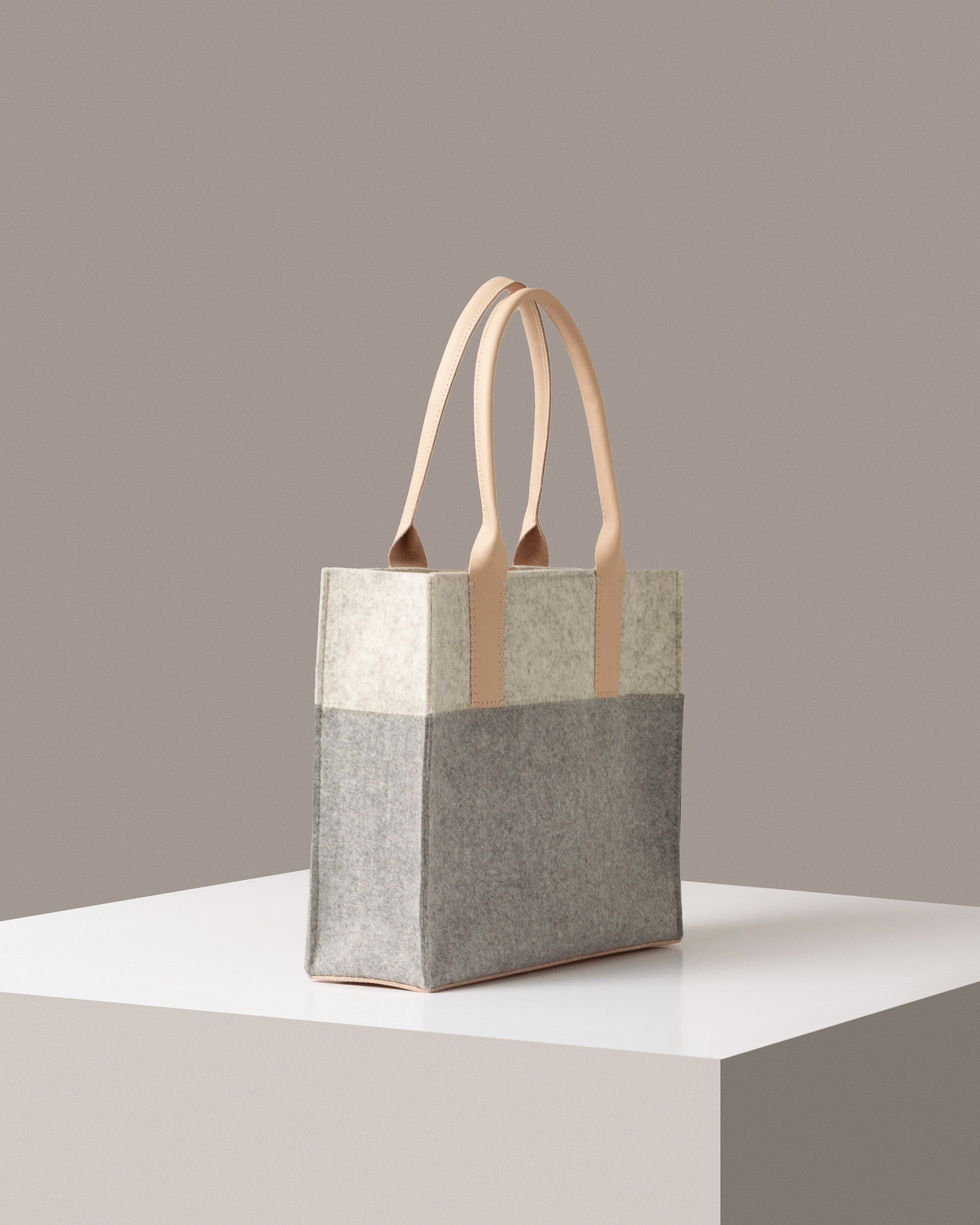 A Jaunt Midi Merino Wool Felt Tote in white, gray, and beige colors on a white base displayed in a side-view