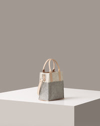 A Jaunt Mini Merino Wool Felt Crossbody bag in white, gray, and beige colors on a white base displayed in a side-view