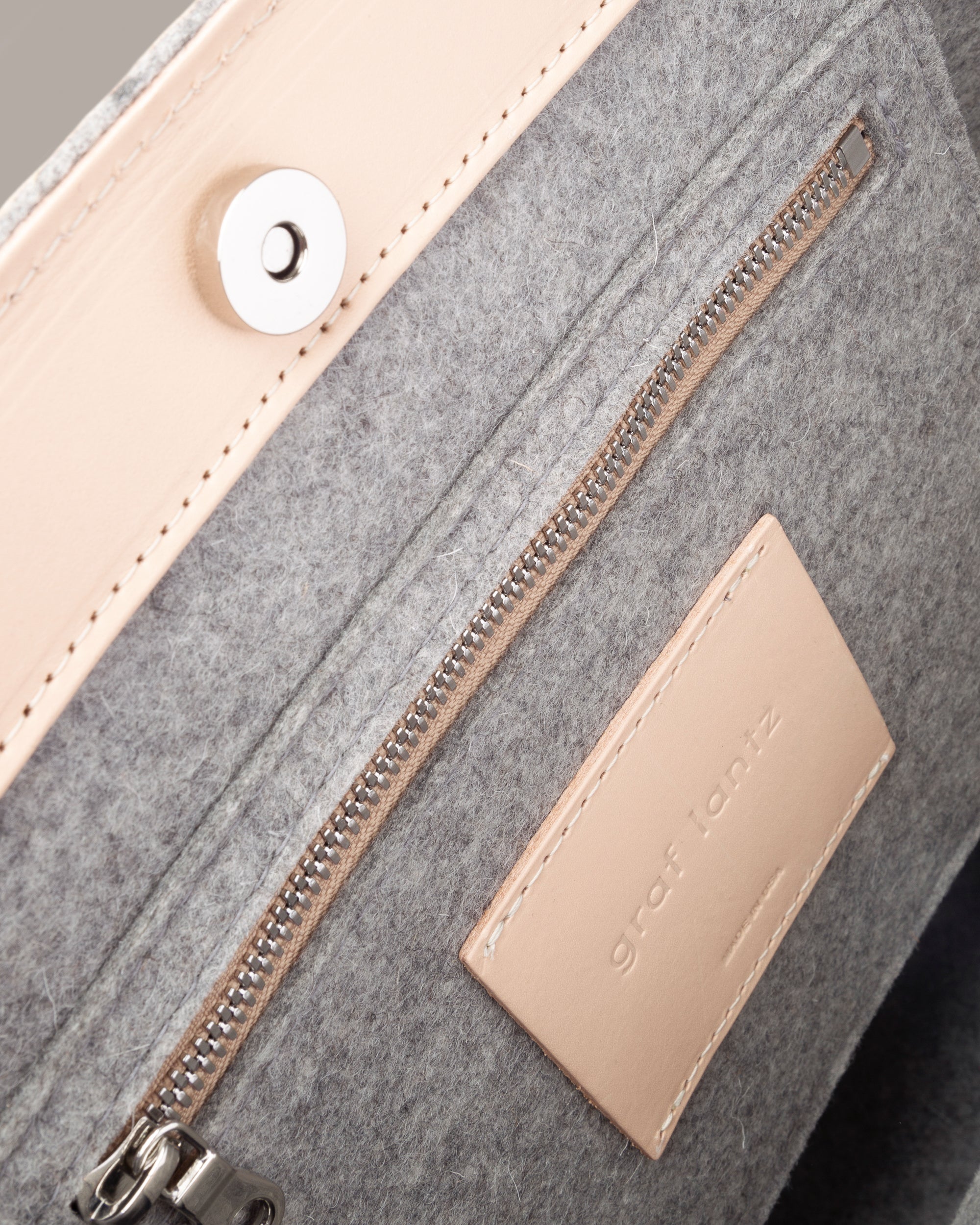 Interior view of a gray Frankie Merino Wool Felt Midi tote featuring a zippered felt pocket, beige leather trim, and nickel hardware, highlighted in detail