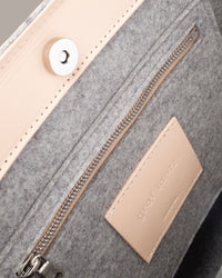 Interior view of a gray Frankie Merino Wool Felt Tote featuring a zippered felt pocket, beige leather trim, and nickel hardware, highlighted in detail