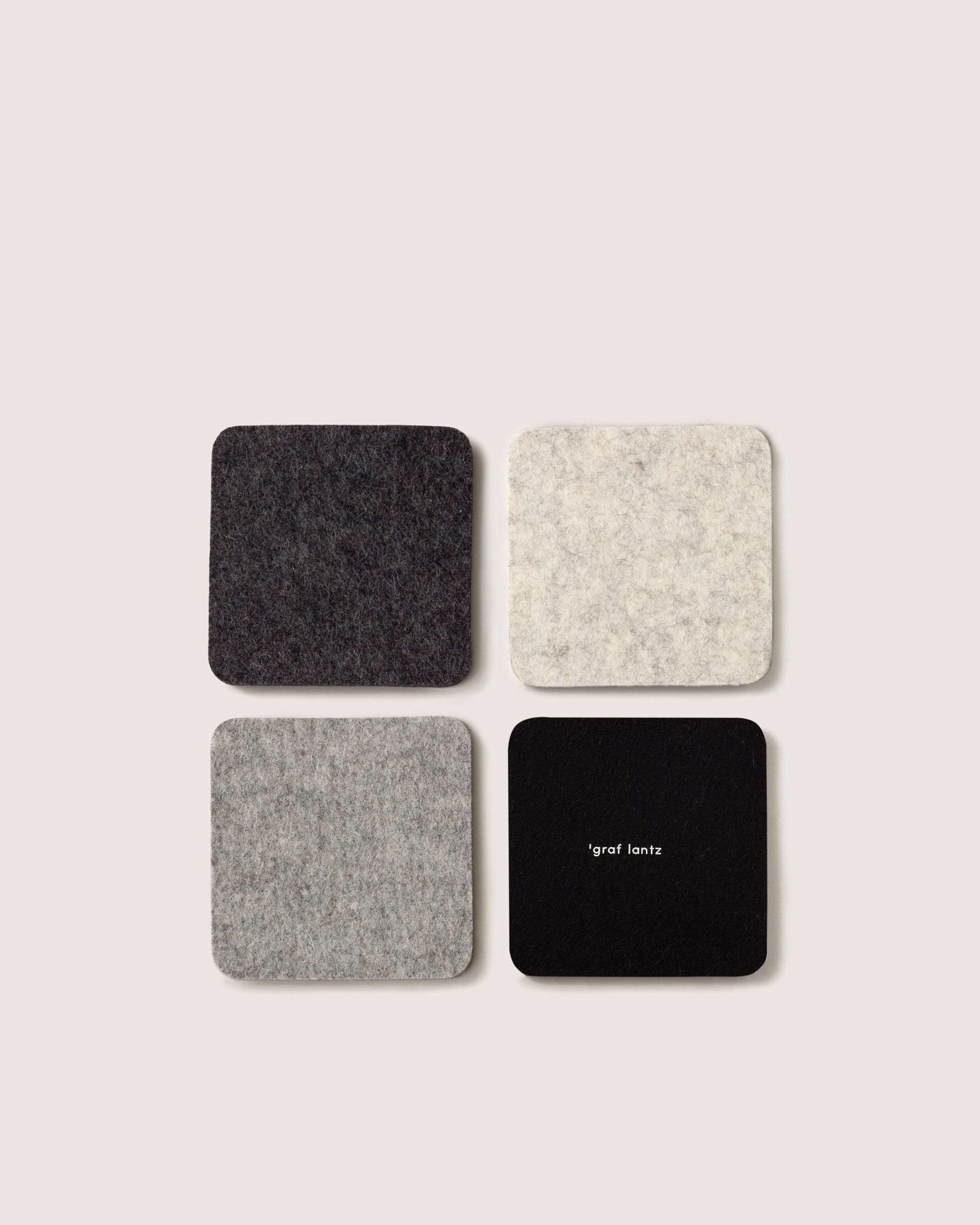 A 2x2 grid displays four square coasters made from German Merino wool in gray and black shades on a light background. The bottom right coaster features graf lantz in small white text, evoking the classic Bierfilzl style.