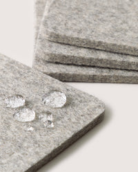 Close-up of gray felt squares by graf lantz, made from German Merino wool. In the foreground, several water droplets rest on one square, showcasing its water-resistant texture.