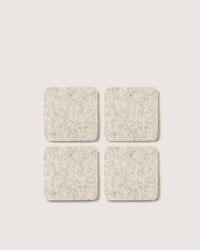 The graf lantz set includes four square, light gray felt coasters made from soft Merino wool. They feature slightly rounded corners and a gentle texture, arranged in a 2x2 grid on a white background, blending functionality with elegance in home décor.