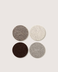 The graf lantz set includes four round Merino wool coasters in light gray, dark gray, dark brown, and beige. Arranged in a two-by-two grid on a plain background, these coasters exemplify sustainable home décor with premium German craftsmanship.