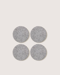 The graf lantz set includes four round, gray felt pads made from soft German Merino wool. These pads add elegance and protect surfaces from scratches, arranged in a square formation on a white background.