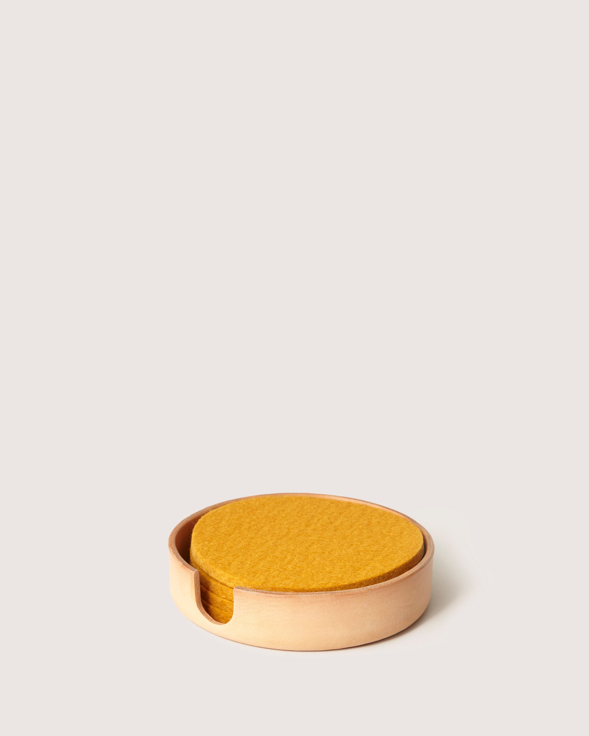 Graf Lantz round, yellow felt coasters neatly stack in a light wooden holder with a notch, offering a charming contrast against the soft neutral backdrop.