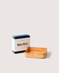A set of vibrant square Bierfilzl coasters made from rich Merino wool accompanies a light brown rectangular tray crafted from Kobon leather by graf lantz on a plain background.