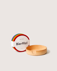 Displayed alongside a light wooden holder, the graf lantz Bierfilzl set consists of colorful Merino wool coasters. Stacked neatly in hues of red, blue, and green, they blend style with eco-conscious living and are crafted from sustainable materials.