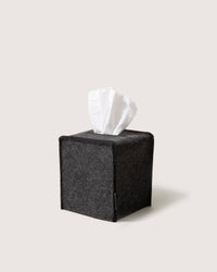 The graf lantz tissue box cover, made from black felt, elegantly displays a single white tissue against a light gray backdrop. This chic accessory complements any home décor with its blend of style and function.