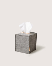 A graf lantz gray Merino wool tissue box cover, featuring tissues extending from the top. This cube-shaped accessory on a simple light backdrop accentuates its plush texture and is Oeko-Tex® Certified for assured elegance and safety.
