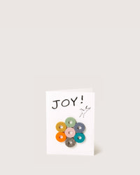 The graf lantz greeting card features JOY! on the front, accented with a textured design of colorful circular shapes and a small doodle of a bird. Set against a plain, light background, its perfect as a host gift.