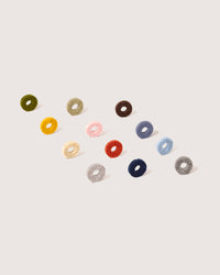 Twelve vibrant, circular felt rings by graf lantz, crafted from Merino wool, form a diagonal pattern on a light background. Each unique Wine-O acts as a stylish wine glass marker in colors such as green, yellow, red, pink, grey, blue, and brown.