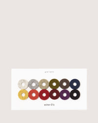 A set of 12 colorful wine glass markers in Merino wool felt, arranged in two rows. Each circle has a central hole. Shades include gray, olive, red, and brown. Elegantly printed below is graf lantz Wine-Os.