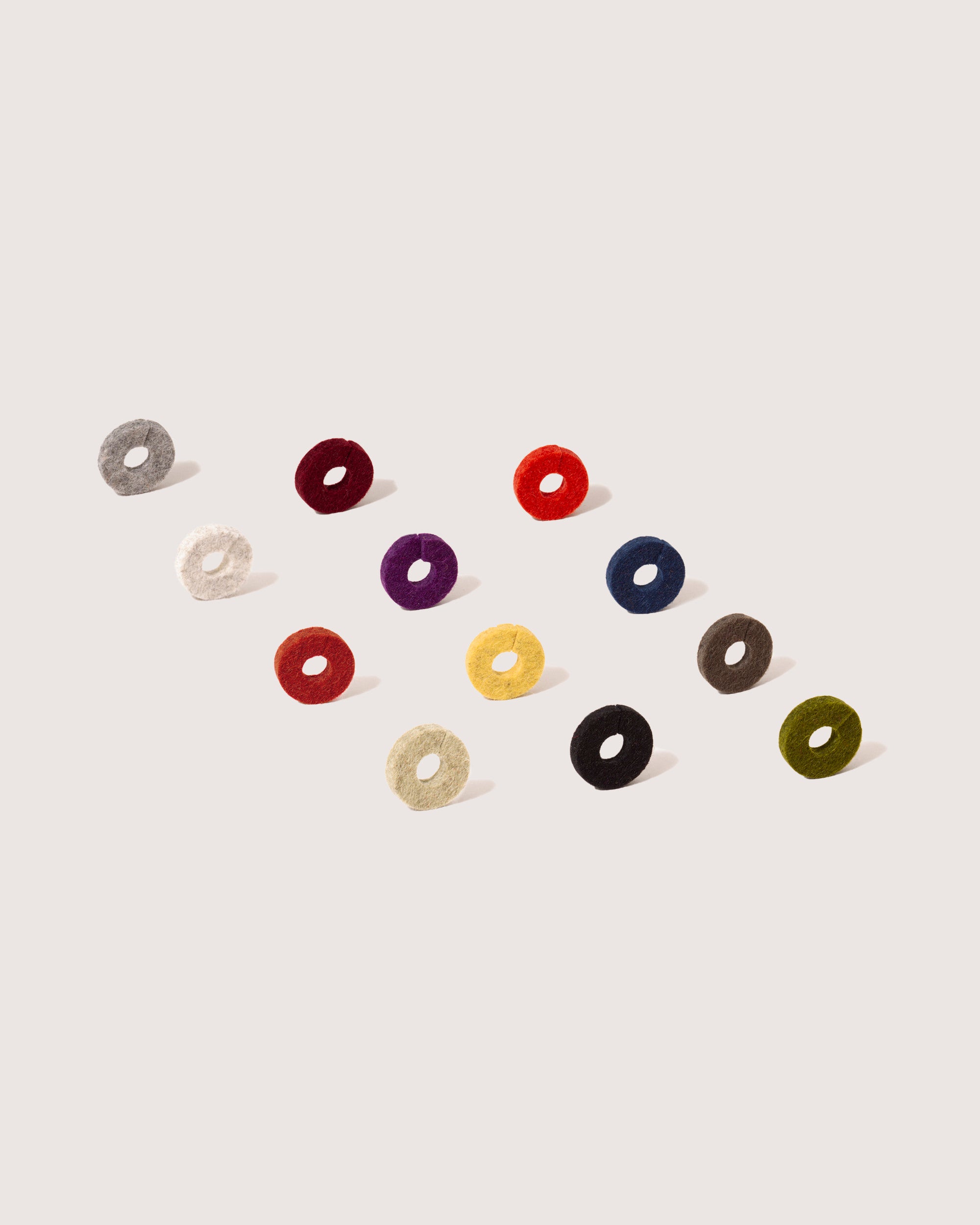 A set of twelve vibrant graf lantz Merino wool felt coasters, ideal for sustainable luxury, is arranged diagonally against a light backdrop. Each coasters distinct color—ranging from gray to red—adds style and serves as elegant wine glass markers.