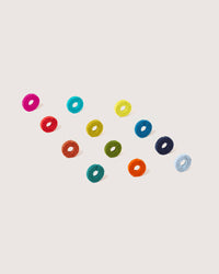 Colorful rings, similar to Wine-Os wine glass markers by graf lantz, adorn the plain background. Made from Bavarian Merino wool felt in bright hues like pink, turquoise, yellow, and red, they create a vibrant and playful composition.