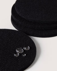 Close-up of Bierfilzl Merino Wool Round Coasters in black, made from German Merino wool, stacked in pairs on a white surface. In the foreground, one coaster is adorned with scattered clear round beads.