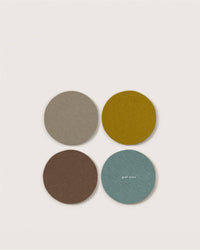 Set of four round Graf Lantz Merino wool coasters in beige, mustard yellow, brown, and light blue, arranged in a square on a light background. Graf Lantz is printed on the bottom right coaster.