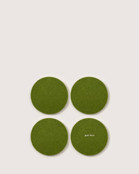 Four green felt coasters, made from German Merino wool and shaped round, are placed in a square on a light background. The coaster at the bottom right prominently features the brand name graf lantz.