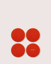Four red circular felt coasters, crafted from luxurious German Merino wool by graf lantz, are set in a square on a white background. One coaster is elegantly printed with graf lantz in small white letters.