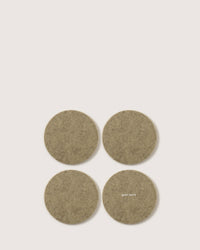 Four round, beige felt coasters made from Oeko-Tex Certified German Merino wool are arranged in a square on a plain background. One coaster showcases the graf lantz logo.