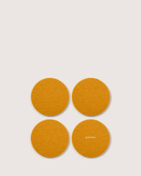 Four orange felt coasters made of German Merino wool, each round and displaying the text graf lantz on the bottom right one, are arranged in a square pattern.