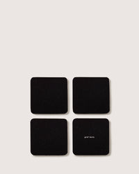 Arranged in a grid on a light background are four black square coasters, each possibly crafted from Merino wool. One of these coasters features the small text graf lantz.