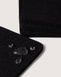 A close-up of the water-resistant black fabric by graf lantz, with droplets beading on its surface. The material, reminiscent of Merino wool, is layered over a similar background piece to highlight its durability and style.