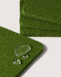 Close-up of stacked green felt coasters by graf lantz on a light surface, featuring three water droplets on the top coaster that showcase the water-resistant texture of German Merino wool.