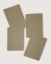 Four beige, rectangular cards from graf lantz lie scattered on a white surface. They feature rounded corners and a textured finish akin to sustainable tableware, designed to elegantly complement eco-friendly dining settings.