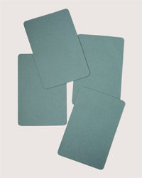 Four blank, green rectangular cards with rounded corners by Graf Lantz are scattered on a plain white background, resembling sustainable placemats ideal for a stylish designer table setting.