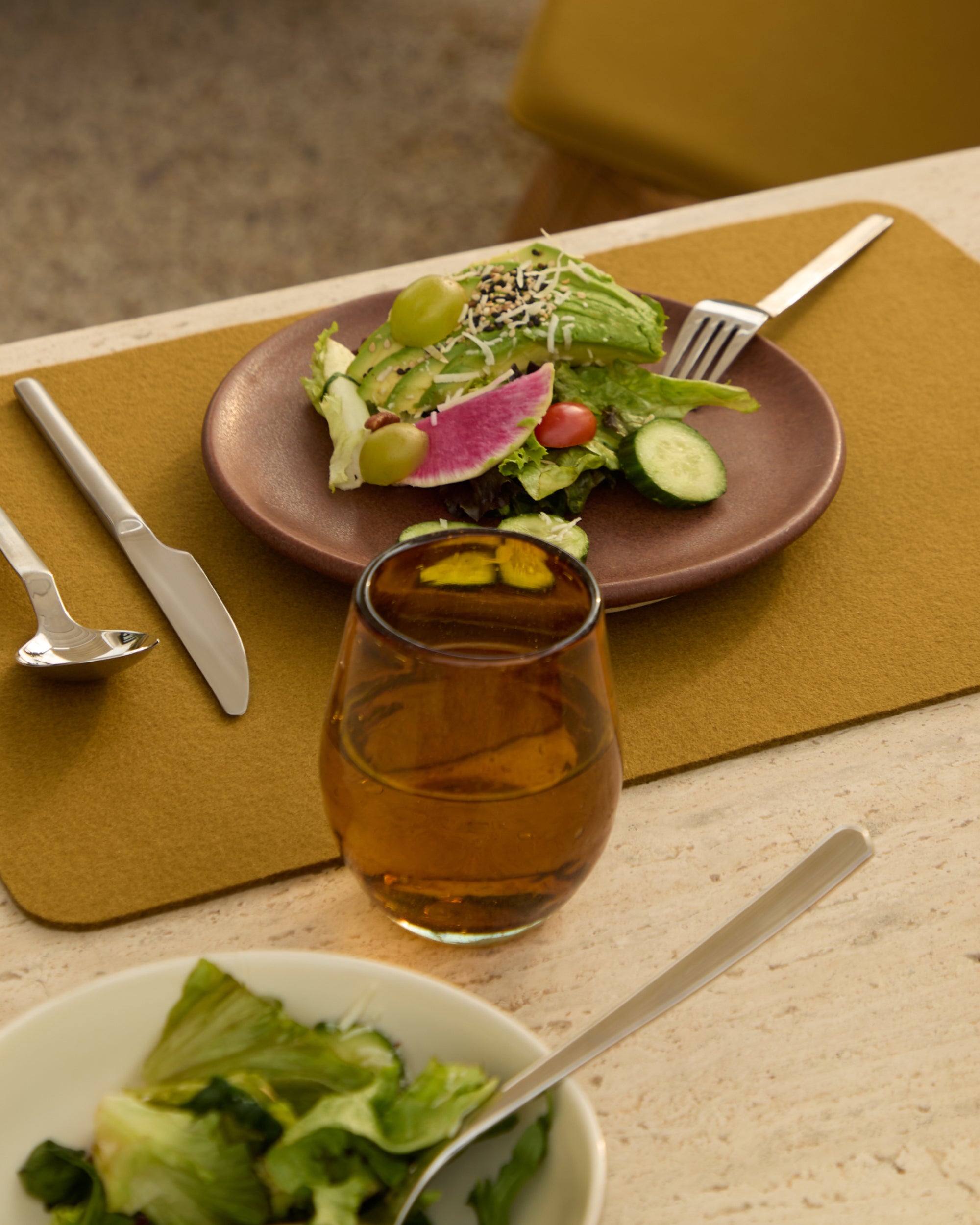 Dinner table setting with a salad plate, glass of iced tea, and cutlery on a placemat.