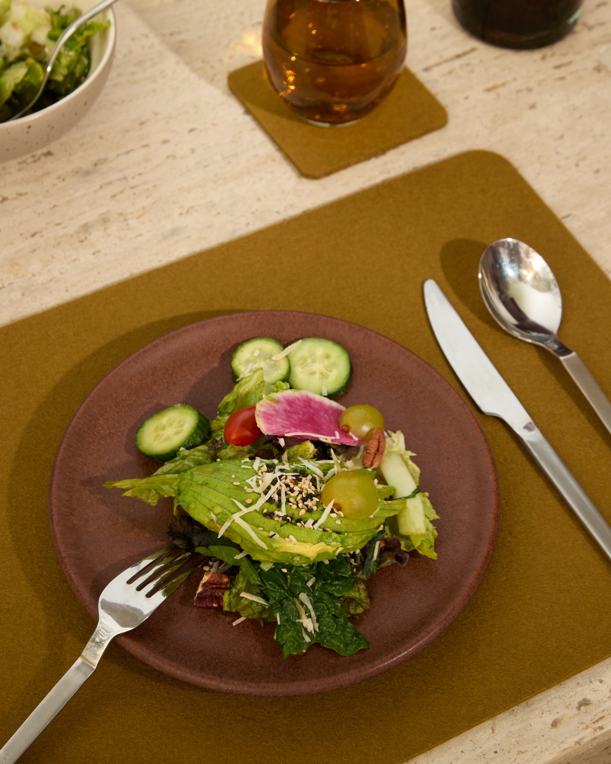 Plated salad with cucumbers, tomatoes, and a watermelon radish on a brown plate with cutlery.
