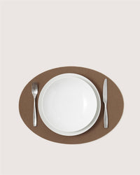 A white plate with a fork on the left and knife on the right, all arranged on a brown Graf Lantz Merino wool placemat set against a light background.