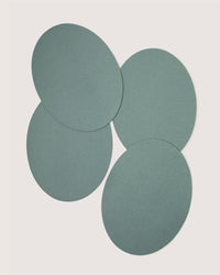 Four overlapping, flat, greenish-blue Merino wool placemats from Graf Lantz are arranged on a plain white background.