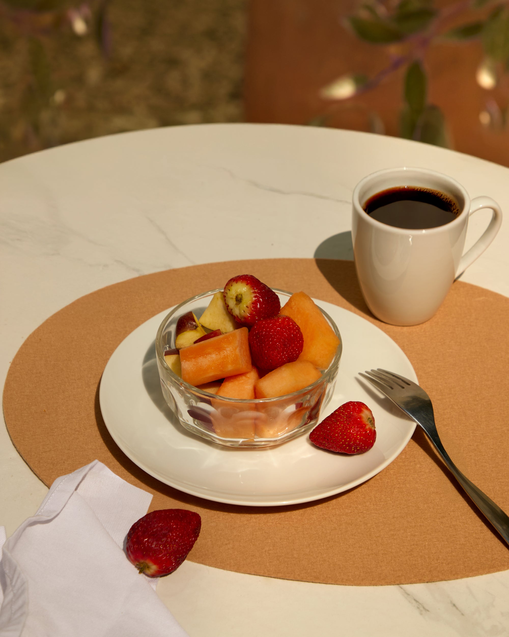 Fruit salad in a glass bowl with a cup of coffee on a table