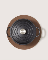 A black cast iron Dutch oven with a silver knob sits on a Graf Lantz sustainable Merino wool trivet, viewed from above against a light background.