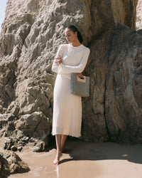 The graf lantz Asobi Bag is a minimalist clutch made from gray Merino wool, with a rectangular cut-out handle reinforced by a beige strap. The lower half features small, evenly spaced holes, all set against a light neutral background for an elegant and simple look.